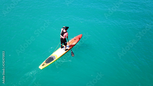Aerial drone bird's eye view of young man exercising sup board in turquoise tropical clear waters