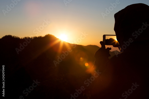A man or woman takes a photo of a beautiful sunrise on his phone. Siluet.