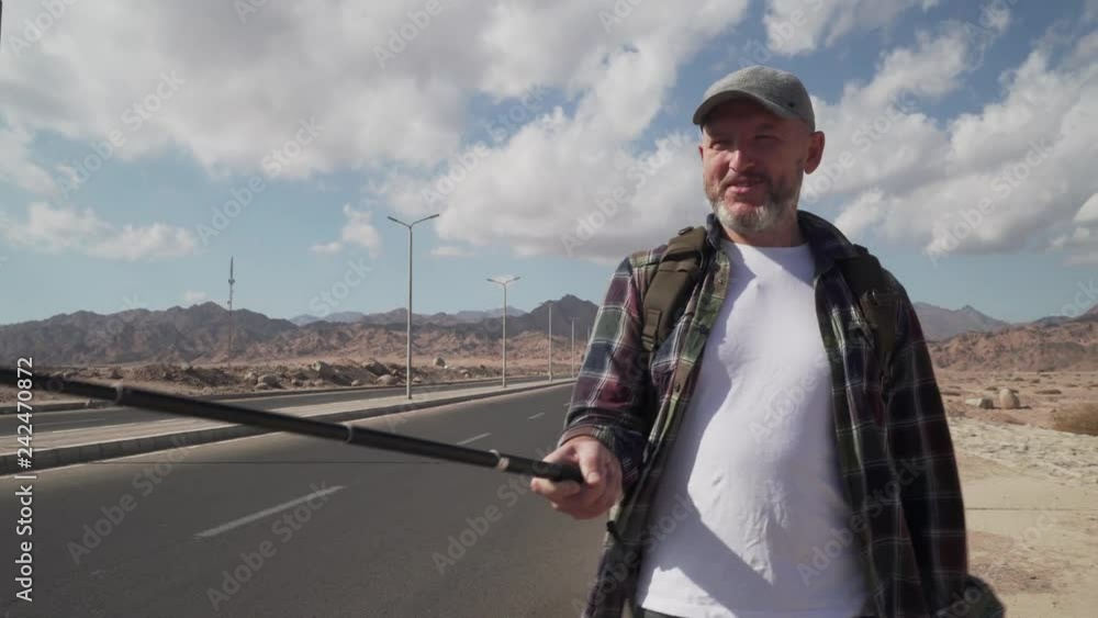Hand-held shot of walking senior traveler male shooting himself with monopod Hand-held shot of walking senior traveler male shooting himself with monopod
