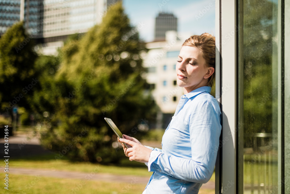Woman leaning against a building holding tablet Woman leaning against a building holding tablet