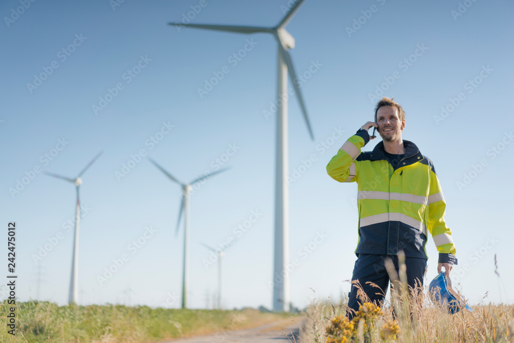 Smiling engineer standing in a field at a wind farm talking on cell phone