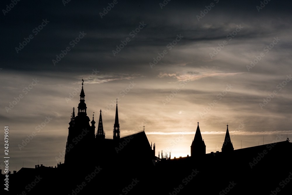 Dramatic cityscape silhouette at sunset from Prague, Czech Republic with the St. Vitus cathedral against the setting Sun. Heavy summer evening clouds add contrast to the picture 