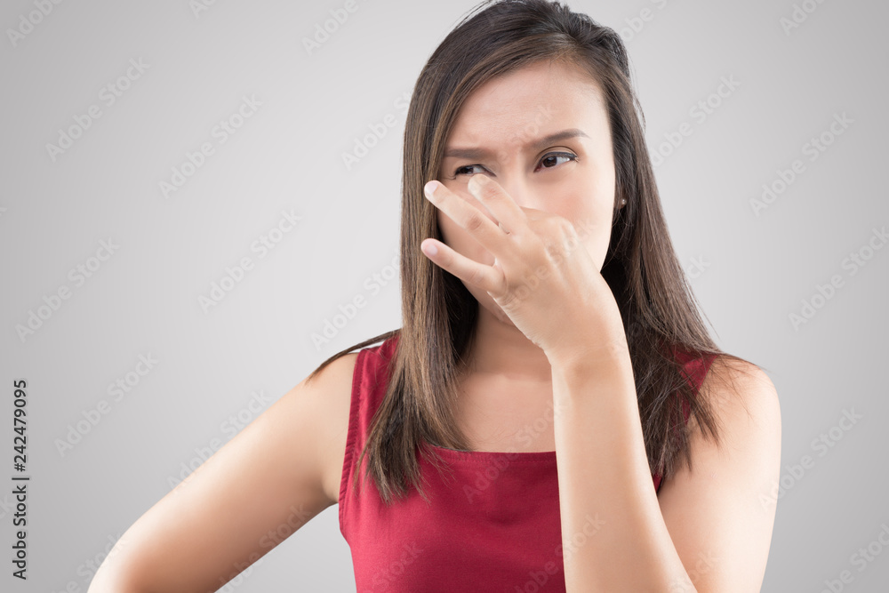 Asian woman in red shirt holding her nose because of a bad smell on gray background. Asian woman in red shirt holding her nose because of a bad smell on gray background.