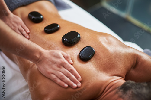 Young man with hot mineral stones on his back receiving spa treatment