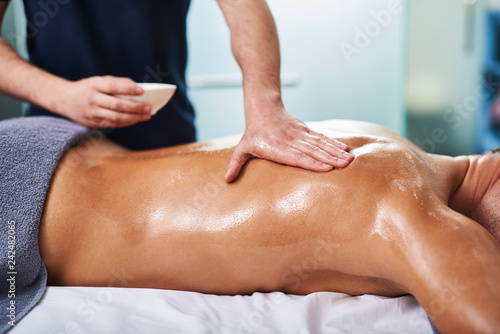 Professional masseur applying massage oil on client back