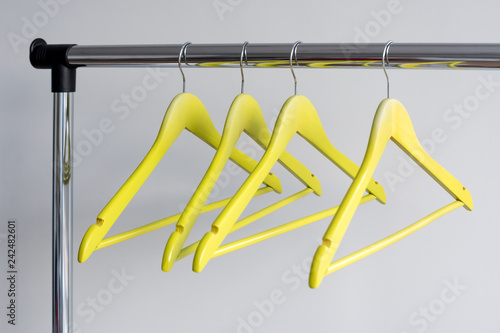 Empty clothes hangers on metal rail against grey background. Rectangular metal clothing rail with empty color wooden coat hangers.