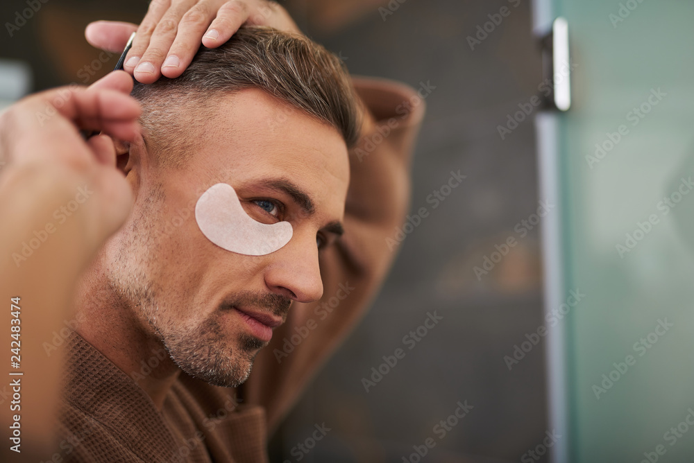 Obraz premium Gorgeous young man with patches under eyes brushing his hair
