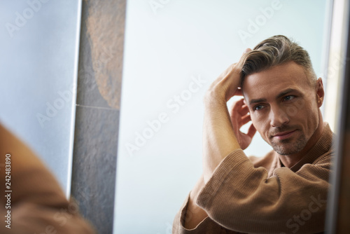 Handsome young man looking in the mirror at bathroom