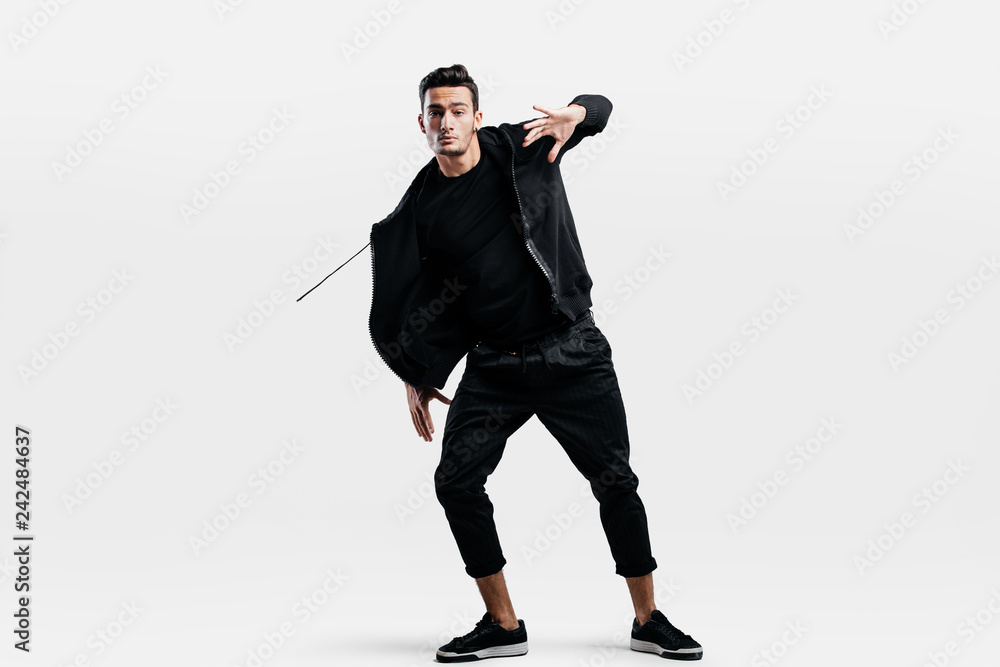 Stylish young man wearing a black sweatshirt and black pants makes stylized movements of hip-poh Stylish young man wearing a black sweatshirt and black pants makes stylized movements of hip-poh