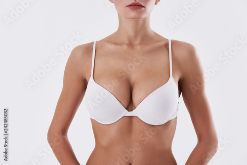 Obraz na plátne Attractive lady with beautiful breast in bra standing against white background