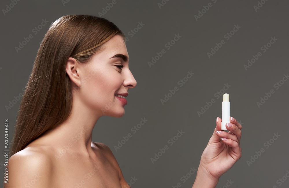 Fototapeta premium Beautiful young lady with naked shoulders holding hygienic lipstick
