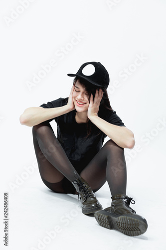 Smiling young dark-haired girl in a black top, tights and cap is sitting on the floor on the white background in studio Stock Photo | Adobe Stock