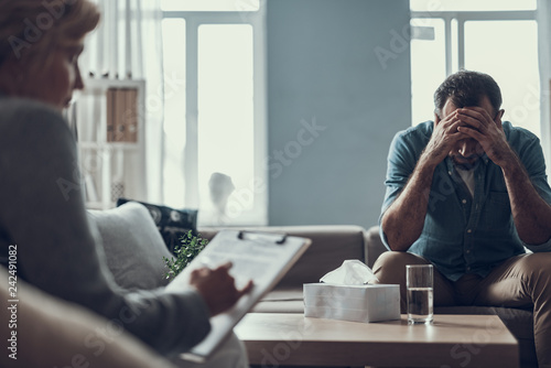 Depressed man hiding his eyes during the session with psychotherapist photo