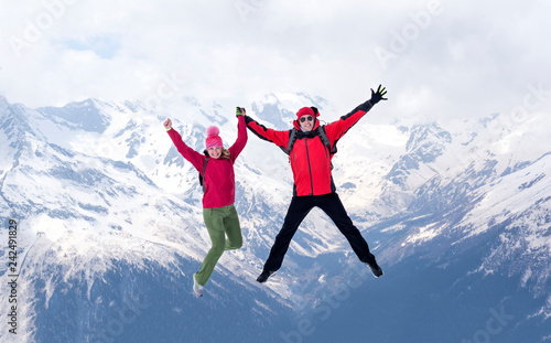 man and a woman in winter jackets jump together against the background of snow-covered mountains, North Caucasus