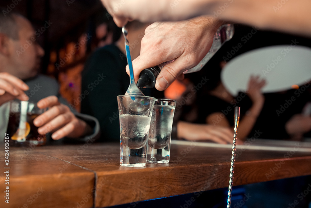 Bartender pouring strong alcoholic drink into small glasses on bar. Red shots at the nightclub. Red alcoholic drink in glasses on bar. Red cocktail at the nightclub. Barman preparing cocktail shooter