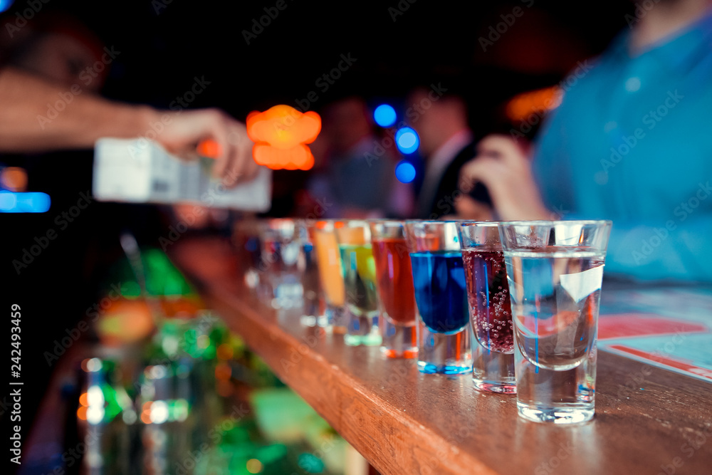Bartender pouring strong alcoholic drink into small glasses on bar. Red shots at the nightclub. Red alcoholic drink in glasses on bar. Red cocktail at the nightclub. Barman preparing cocktail shooter Bartender pouring strong alcoholic drink into small glasses on bar. Red shots at the nightclub. Red alcoholic drink in glasses on bar. Red cocktail at the nightclub. Barman preparing cocktail shooter