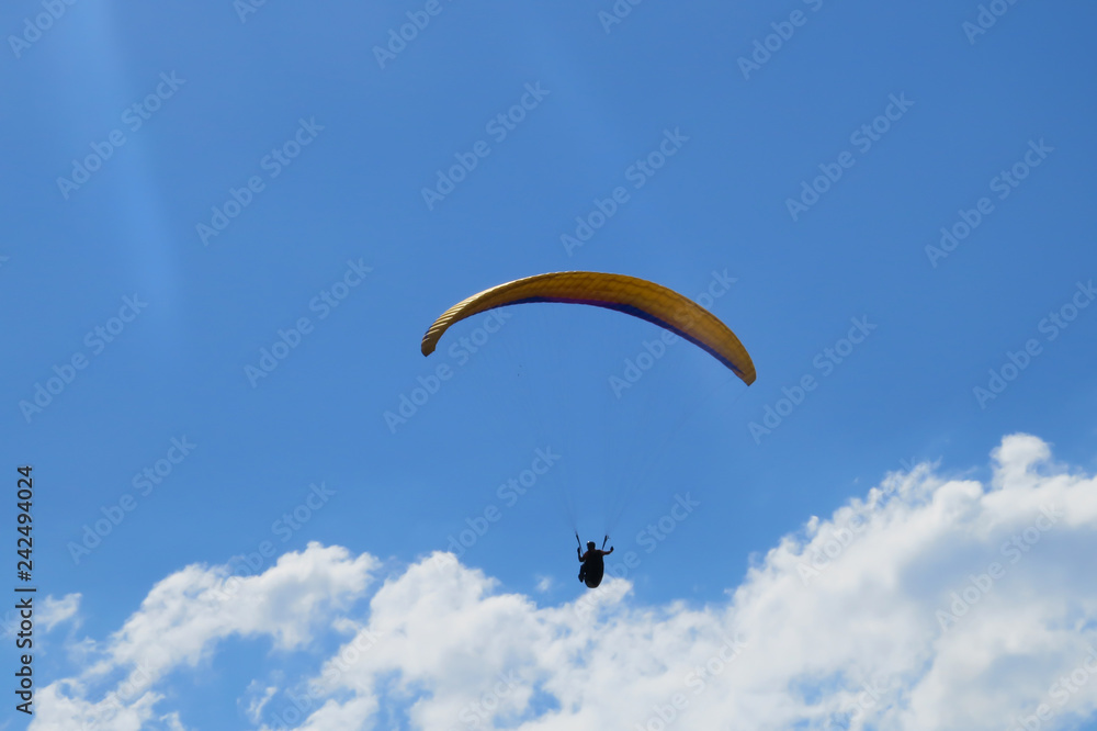 Paraglider flying on colored parachute in blue clear sky at a bright sunny summer day. Active lifestyle, extreme hobbies Paraglider flying on colored parachute in blue clear sky at a bright sunny summer day. Active lifestyle, extreme hobbies