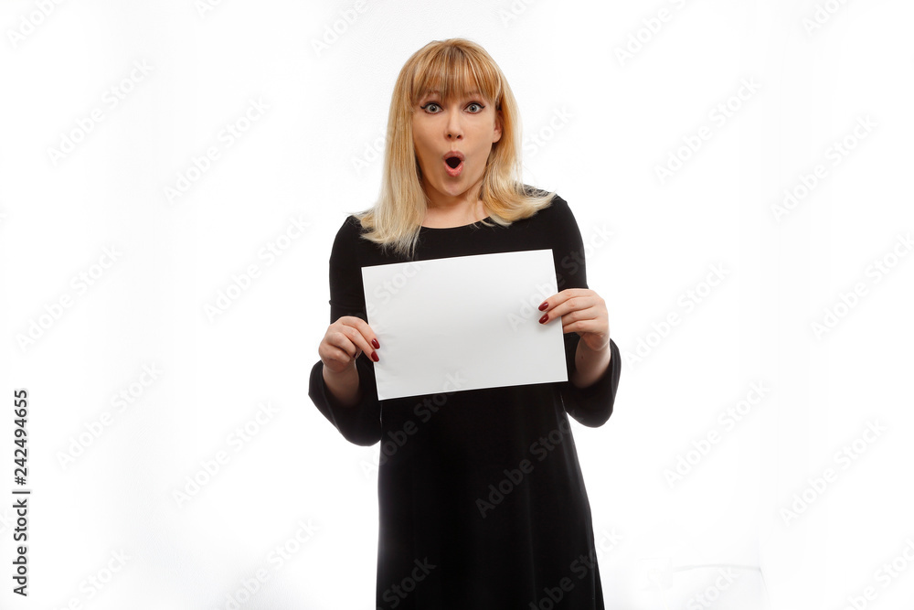 Surprised blonde model in a black dress with a sheet for the text in the hands on a white background. Emotions model. Surprise and invitation. Place for text. A model mouth open. Strong surprise Surprised blonde model in a black dress with a sheet for the text in the hands on a white background. Emotions model. Surprise and invitation. Place for text. A model mouth open. Strong surprise