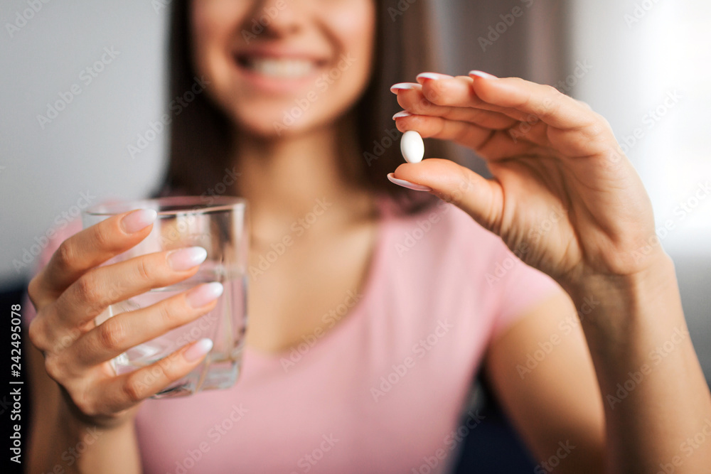 Cut view of young positive woman hold white pill and glass of water. She smiles to camera. Cut view of young positive woman hold white pill and glass of water. She smiles to camera.
