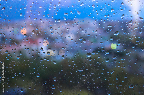 Raindrops on window glasses surface with blurred cityscape background