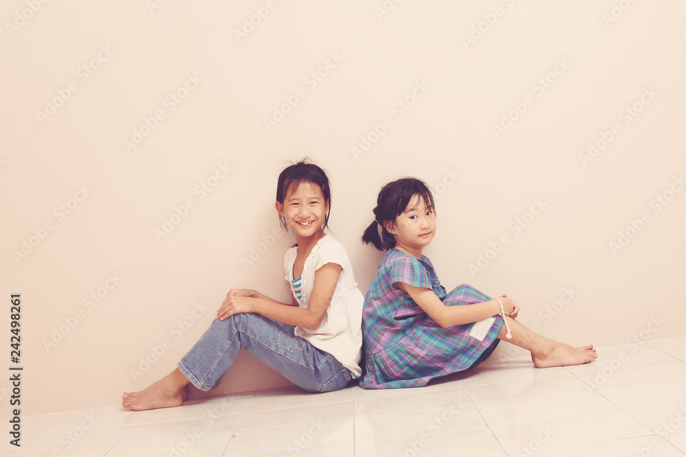 Cute smiling asian siblings sit and touch each other with their backs. Lovely sincere emotions from childhood. Cute smiling asian siblings sit and touch each other with their backs. Lovely sincere emotions from childhood.