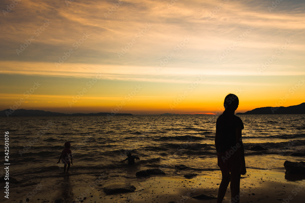 Child playing with sun is hiding the beach edge with orange sky