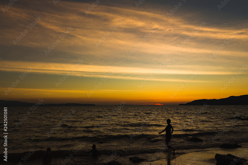 Child playing with sun is hiding the beach edge with orange sky Child playing with sun is hiding the beach edge with orange sky
