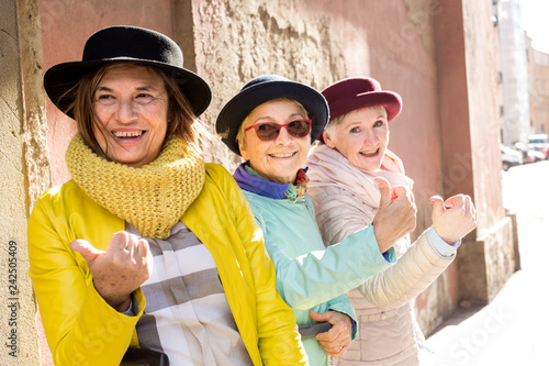 Tre amiche di età matura in viaggio con il cappellino fanno l'autostop sorridendo photo