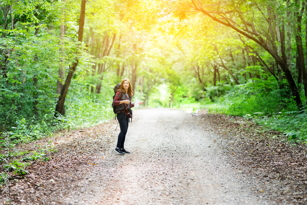 Obraz premium Hipster Asian young girl with backpack enjoying forest on mountain.Tourist traveler with trendy look searching direction on location map , Greenfield. Hiker looking sunlight in trip in the countryside