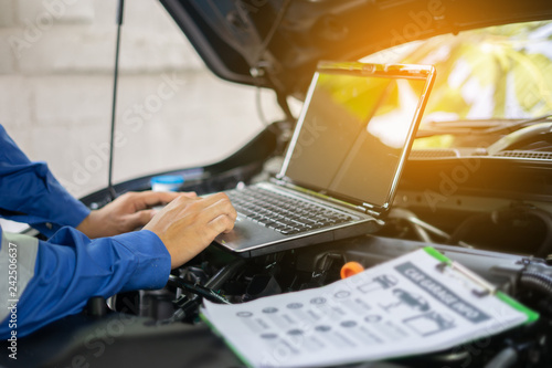 car service, repair, maintenance  concept - auto mechanic man or Smith writing to the clipboard at warehouse workshop, technician doing the checklist for repairs engine a car in the garage with laptop