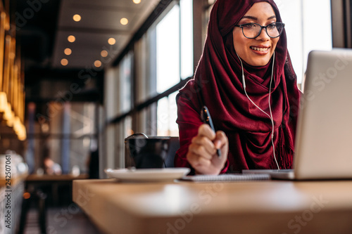 Canvas Print Female in hijab at cafe having video conference on her laptop