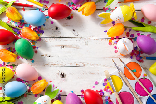Easter background with eggs, tulips and confetti on white wooden background. Top view. Copyspace