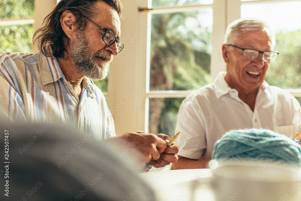 Obraz premium Senior beard man knitting with friend sitting by