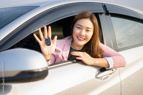 Photography Asian driver woman smiling and showing new car key while sitting in a car that she taking it from dealer in the auto show