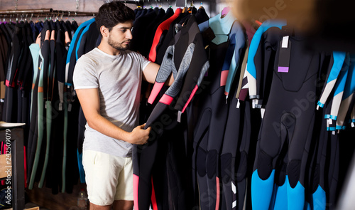 man holding and choosing suit for surfing in the shop