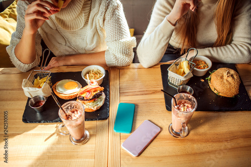 Cut view of table full of food and drink. There are young women sit at table. Two phones lying there. Models eating.