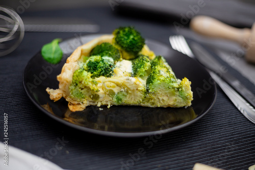 Slice of tart with broccoli and baked cheese sauce on black plate