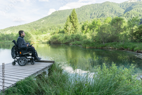 Obraz na plátne Disabled man on wheelchair enjoying and looking at beautiful nature on lake pier