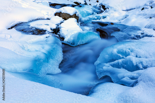 Mountain river in winter time in a frozen blue ice and pure snow