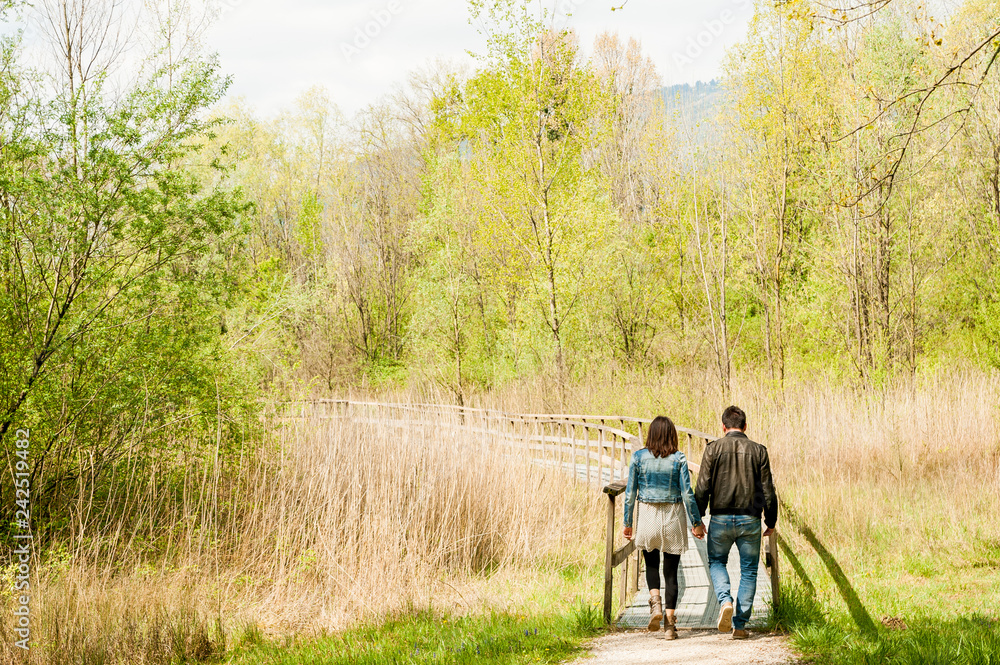 young couple, dressed in modern casual way, walking on wooden pier during sunny day in the woods, immersed in nature young couple, dressed in modern casual way, walking on wooden pier during sunny day in the woods, immersed in nature