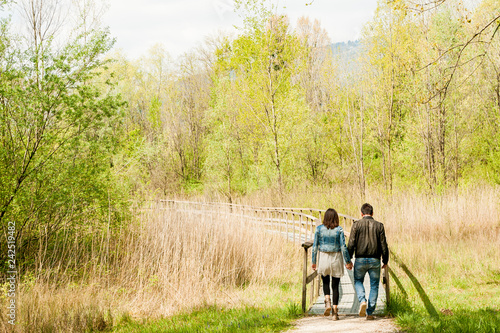 young couple, dressed in modern casual way, walking on wooden pier during sunny day in the woods, immersed in nature