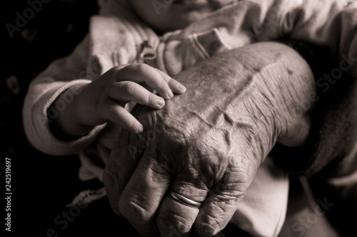 small baby hand touching and caressing old grandmother hand with wrinkles, symbol of passing generations