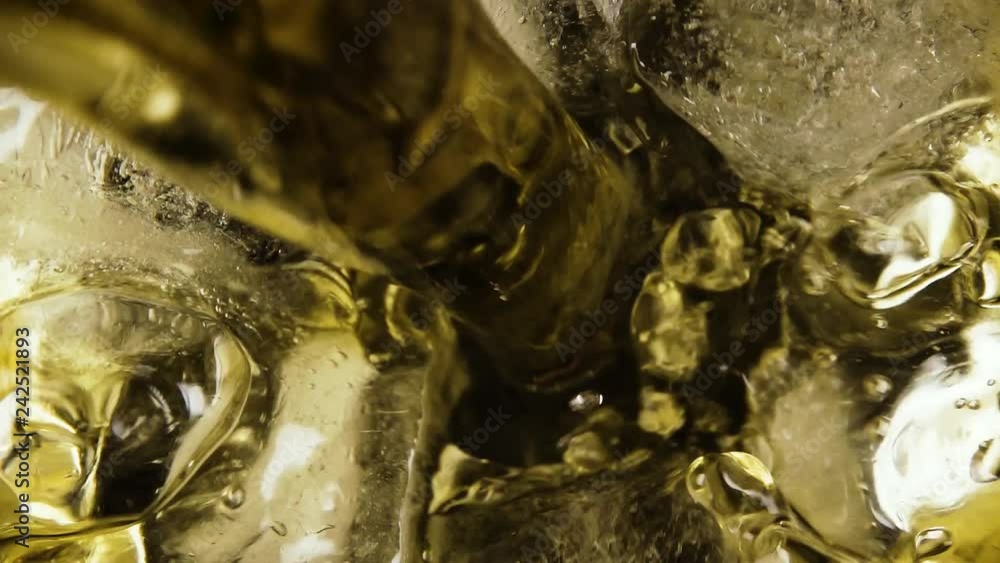 Slow motion natural transparent ice cubes in a glass pour brown alcoholic drink top view