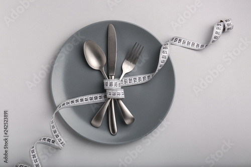 Plate and cutlery tied with measuring tape on grey background. Diet concept