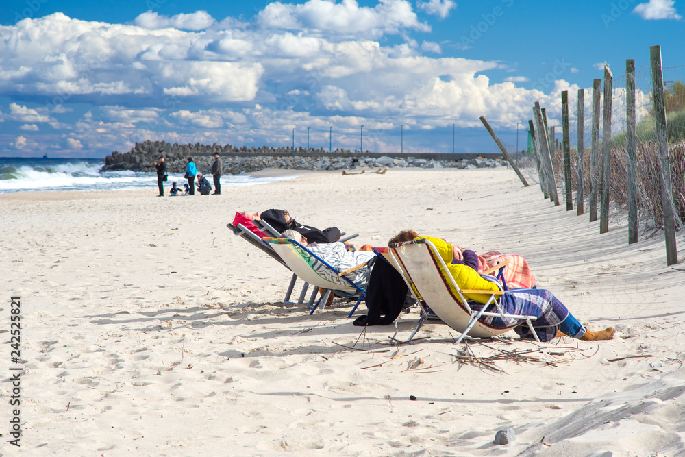 Friends on chairs taking sun bath in winter at the Baltic Sea beach Friends on chairs taking sun bath in winter at the Baltic Sea beach