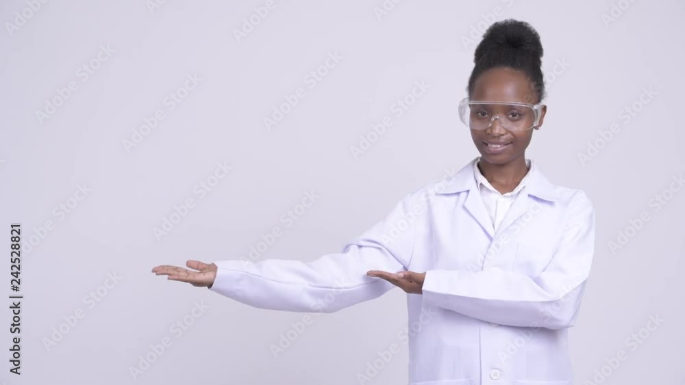 Young happy African woman doctor with protective glasses showing something Young happy African woman doctor with protective glasses showing something