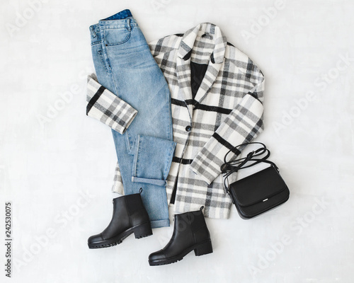 Blue jeans, striped coat, small black cross body bag and leather ankle boots on grey background. Overhead view of woman's casual day outfits. Trendy hipster look. Flat lay. photo