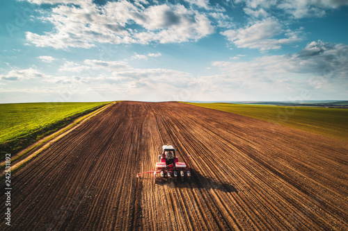 Farmer with tractor seeding crops at field, aerial view