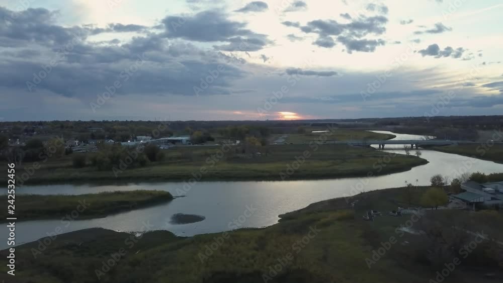 Aerial view of a small town by the river during a vibrant cloudy sunset. Taken in Brandon, Manitoba, Canada. Aerial view of a small town by the river during a vibrant cloudy sunset. Taken in Brandon, Manitoba, Canada.