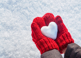 Female hands in knitted mittens with heart of snow in winter day. Love concept. Valentine day background.